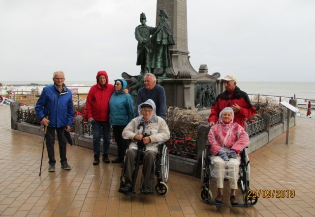 Auf diesem Bild stehen die Teilnehmer vor einem großen Denkmal. Trotz Regen haben sie ein Lächeln in ihren Gesichtern.