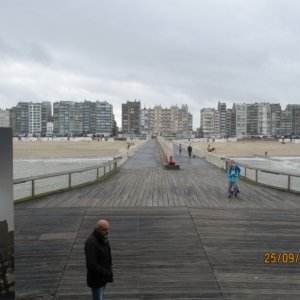 Der Fotograf befindet sich auf dem bekannten Holzsteg in Blankenberge. Er fotografiert Richtung Strand. Man sieht die Wohnblocks am Strand. Links und rechts vom Steg ist das Meer.